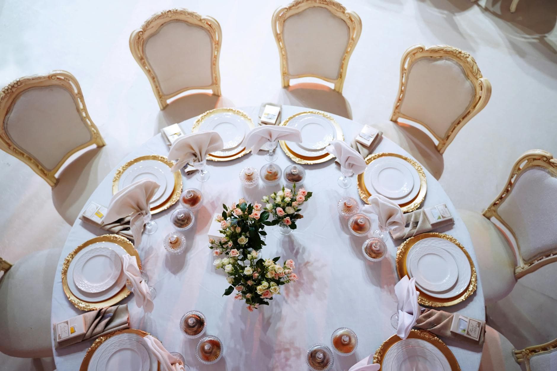 Top-down view of a round event table with gold-rim chargers and ornate chairs